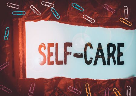 Handwriting text Self Care. Conceptual photo practice of taking action to preserve or improve ones own health Paper clip and torn cardboard placed above a plain pastel table backdropの写真素材