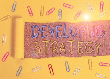Text sign showing Developing Strategy. Business photo text Game plan that sets specific goals and objectives Paper clip and torn cardboard placed above a wooden classic table backdropの写真素材