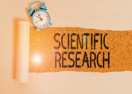 Writing note showing Scientific Research. Business concept for methodical study to prove or disprove a hypothesis Alarm clock and torn cardboard on a wooden classic table backdropの写真素材