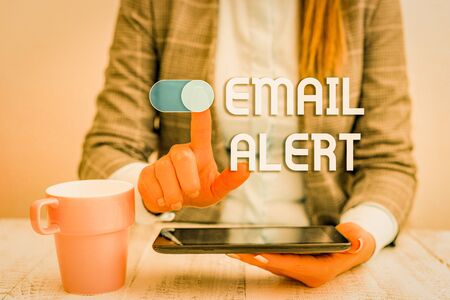 Text sign showing Email Alert. Business photo text emails auto generated nd sent to designated recipients Business woman sitting with mobile phone and cup of coffee on the tableの写真素材