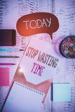 Text sign showing Stop Wasting Time. Business photo showcasing advising demonstrating or group start planning and use it wisely Envelop speech bubble smartphone sheet pens spiral notepads clips woodenの写真素材