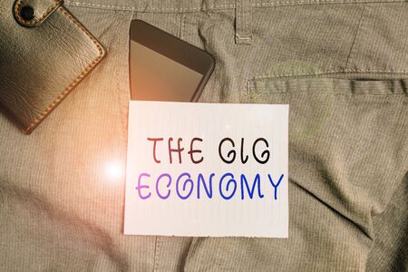 Conceptual hand writing showing The Gig Economy. Concept meaning Market of Shortterm contracts freelance work temporary Smartphone device inside trousers front pocket with walletの写真素材