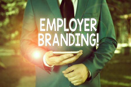 Conceptual hand writing showing Employer Branding. Concept meaning promoting company employer choice to desired target group Businessman in blue suite stands with mobile phone in handsの写真素材