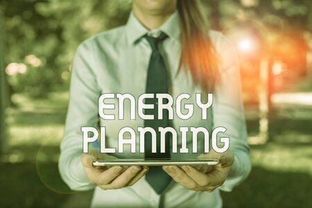 Text sign showing Energy Planning. Business photo showcasing making of a strategy and plan for the consumption of energy Business woman in shirt with a tie holding lap top mobile phone in the handの写真素材