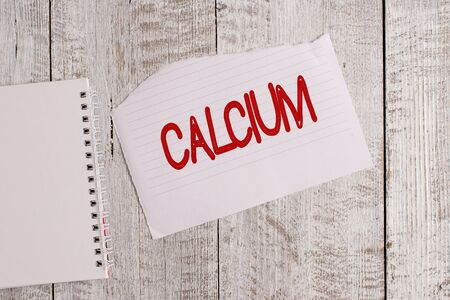 Conceptual hand writing showing Calcium. Concept meaning fifth most abundant element in the human body Silverwhite metal Torn paper and notebook sheet placed above classic wooden tableの写真素材