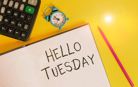 Writing note showing Hello Tuesday. Business concept for a greeting or warm welcome to the third day of the week Open striped notebook calculator metal alarm clock color backgroundの写真素材