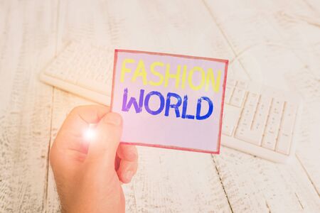 Word writing text Fashion World. Business photo showcasing world that involves styles of clothing and appearance man holding colorful reminder square shaped paper white keyboard wood floorの写真素材