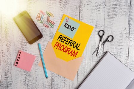 Word writing text Referral Program. Business photo showcasing internal recruitment method employed by organizations Envelope sheet smartphone notes pen notepad clips scissors wooden backの写真素材