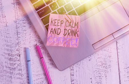 Conceptual hand writing showing Keep Calm And Drink Coffee. Concept meaning encourage to enjoy caffeine drink and relax Metallic laptop crushed colored paper note pens lying wooden table