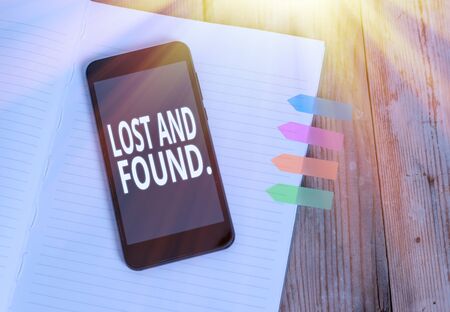 Writing note showing Lost And Found. Business concept for a place where lost items are stored until they reclaimed Striped note book colored arrow banners smartphone wooden backgroundの写真素材