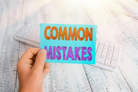 Handwriting text writing Common Mistakes. Conceptual photo actions that are often used interchangeably with error man holding colorful reminder square shaped paper white keyboard wood floorの写真素材
