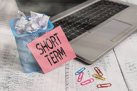 Conceptual hand writing showing Short Term. Concept meaning occurring over or involving a relatively short period of time Metallic laptop sticky note bin paper clips vintage tableの写真素材