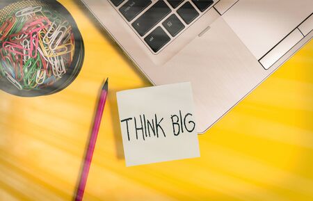 Handwriting text writing Think Big. Conceptual photo To plan for something high value for ones self or for preparation Metallic laptop sticky note clips container pencil colored backgroundの写真素材