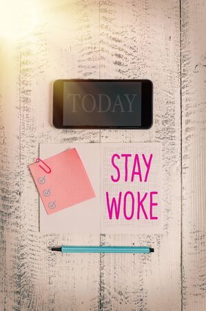 Conceptual hand writing showing Stay Woke. Concept meaning being aware of your surroundings and things going on Keep informed Squared notebook marker smartphone sticky note wooden backgroundの写真素材