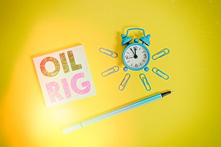 Writing note showing Oil Rig. Business concept for large structure with equipment to remove oil from under the seabed Metal alarm clock wakeup clips ballpoint notepad colored backgroundの写真素材