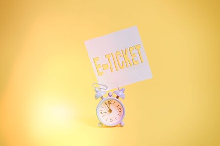 Word writing text E Ticket. Business photo showcasing Digital ticket that is as valid as a paper ticket or its equivalent Metal retro vintage alarm clock blank sticky note sheet colored backgroundの写真素材