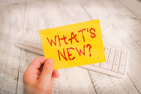 Conceptual hand writing showing What S New Question. Concept meaning Asking about latest Updates Trends Happening News Man holding colorful reminder square shaped paper wood floor