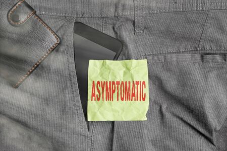 Handwriting text writing Asymptomatic. Conceptual photo a condition or an individual producing or showing no symptoms Smartphone device inside trousers front pocket with wallet and note paperの写真素材