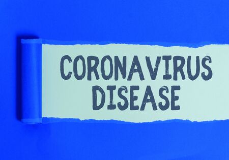 Text sign showing Coronavirus Disease. Business photo text defined as illness caused by a novel virus SARSCoV2 Rolled ripped torn cardboard placed above a wooden classic table backdropの写真素材