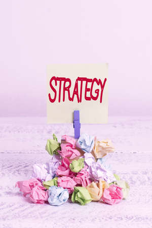 Word writing text Strategy. Business photo showcasing action plan or strategy designed to achieve an overall goal Reminder pile colored crumpled paper clothespin reminder white wooden spaceの写真素材