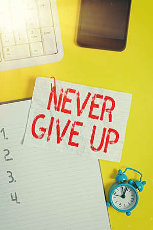 Handwriting text writing Never Give Up. Conceptual photo be persistent to keep on trying to improve the condition Crumpled white paper on table with paper clips clock mobile and pc keyboardの写真素材