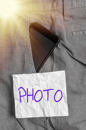 Text sign showing photo. Business photo text defined as produced by light, image taken with the help of light. Smartphone device inside formal work trousers front pocket near note paperの写真素材