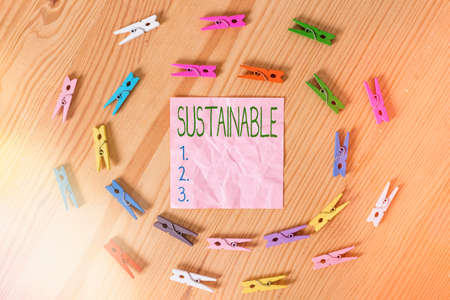 Conceptual hand writing showing Sustainable. Concept meaning the ability to be sustained, supported, upheld, or confirmed Colored crumpled papers wooden floor background clothespinの写真素材