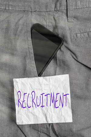 Text sign showing Recruitment. Business photo text action of finding new possible employee to join organization or support Smartphone device inside formal work trousers front pocket near note paperの写真素材