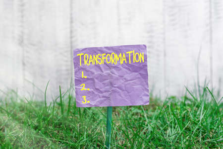 Conceptual hand writing showing Transformation. Concept meaning process, or instance of transforming or being transformed Plain paper attached to stick and placed in the grassy landの写真素材