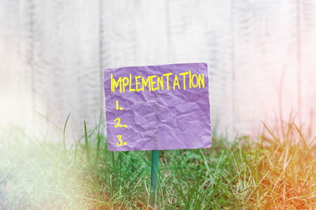 Conceptual hand writing showing Implementation. Concept meaning application of making something active or effective Plain paper attached to stick and placed in the grassy landの写真素材