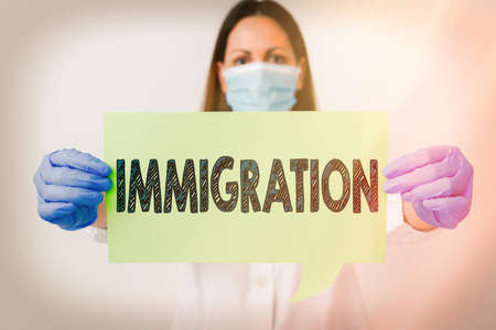 Handwriting text Immigration. Conceptual photo the action of coming to live permanently in a foreign country Laboratory technician featuring empty sticker paper accessories smartphoneの写真素材
