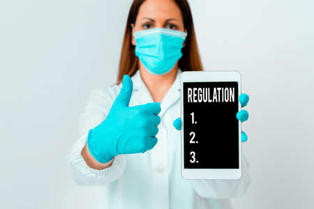 Conceptual hand writing showing Regulation. Concept meaning the authoritative rule dealing with details or procedure Laboratory technician featuring paper accessories smartphoneの写真素材