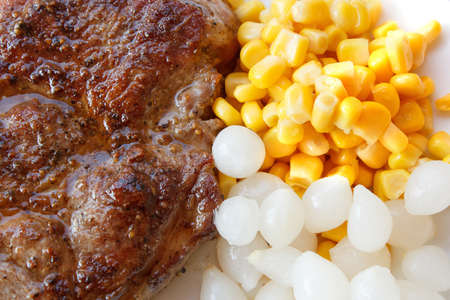 grilled pork steak with corn and small onions on plateの写真素材