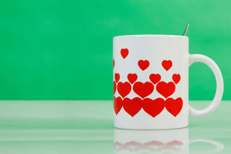 White cup with red hearts on green background