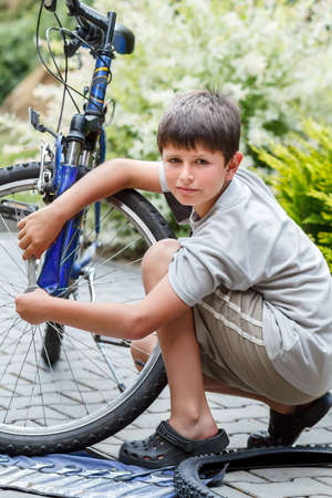 Teenager repairing his bike, using spanner to change broken tyre, outdoor shootの写真素材