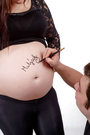 loving happy couple, pregnant woman with her husband, husband writing name of baby to her tummyの写真素材