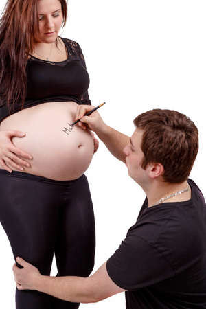 loving happy couple, pregnant woman with her husband, husband writing name of baby to her tummyの写真素材