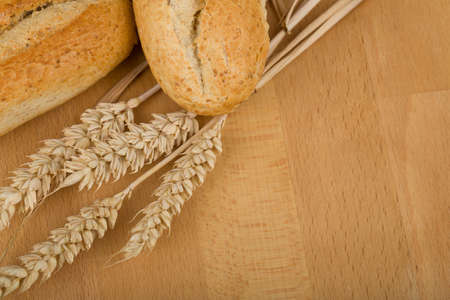 Freshly baked traditional roll on wooden table with ears of wheat grainの写真素材