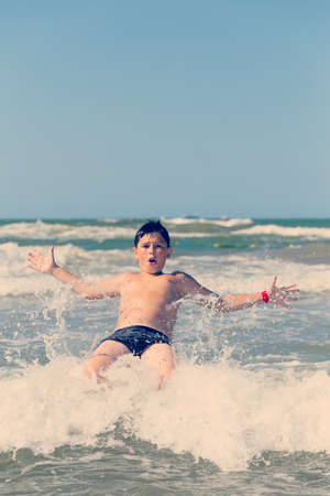Happy boy running and jumping at shallow sea water, retro color toneの写真素材