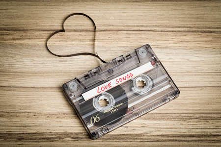 Audio cassette tape on wooden backgound. Film shaping heart, Valentine postcard. Label text love songs.の写真素材