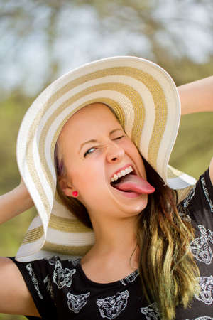 Portrait of grimace cheerful fashionable woman in stylish hat and frock. Crazy happy brunette girl with long hair in warm spring dayの写真素材