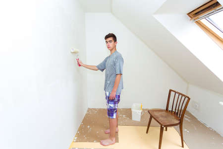 happy young teenager painting wall to white at homeの写真素材