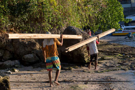 BALI, NUSA PENIDA ISLAND, INDONESIA - JULY 27.2015: Men transports cargo from ship to the shipyard in the hands. There is no other possibility to transport. Nusa Penida July 27. 2015 Indonesiaのeditorial素材