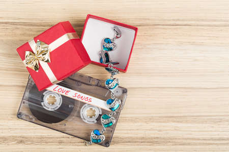 Audio cassette tape with bracelet and present box, label text love songs on wooden backgound....