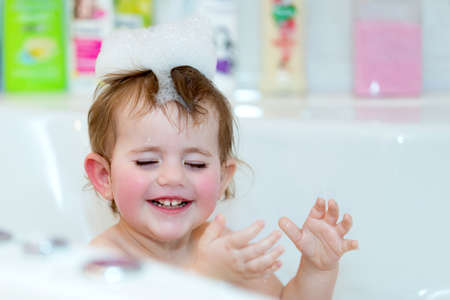 Happy cute little girl taking spa bath at home in water with foam and bubblesの写真素材
