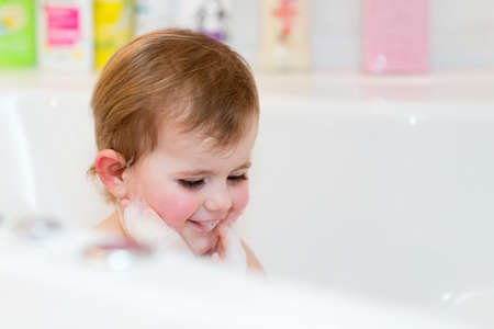 Happy cute little girl taking spa bath at home in water with foam and bubbles