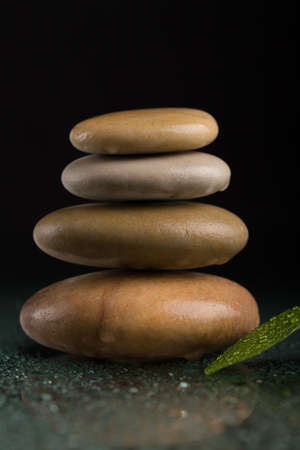 Pile of balancing pebble stones and green leaf with water drop, ZEN stone, on black background, spa...