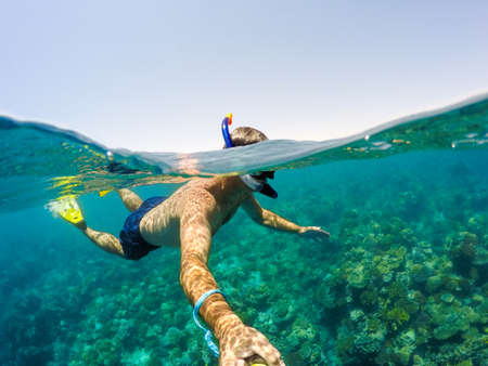 Underwater and surface split view in the tropics paradise with snorkeling man, fish and coral reef, under and above waterline, beautiful view on tropical sea. Safaga, Egypt. Holiday snorkeling vacation conceptの写真素材
