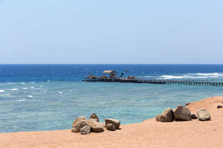 red sea in Egypt coastline with sand and stones and diving pier in background. Tranquil scene with blue water and skyの写真素材