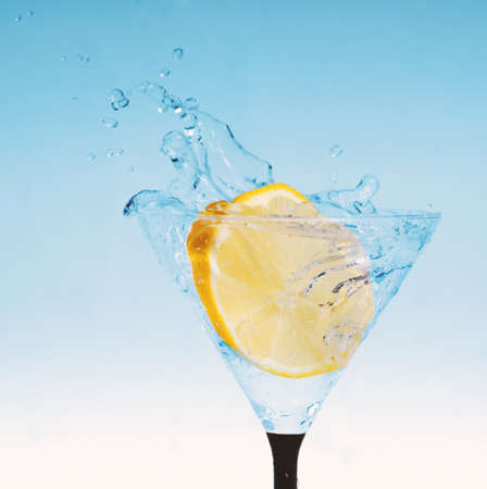 Fresh lemon in glass with sparkling water splash with light blue backgroundの写真素材